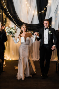 bride-and-groom-walking-down-aisle-with-black-and-white-drape-behind-them