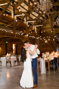 married-couple-kissing-beneath-beautiful-string-lights-and-wood-venue