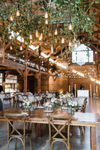 beautiful-metal-frame-with-edison-bulbs-and-greenery-overlooking-dining-hall-with-rustic-wood-tables